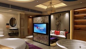 Een moderne hotelkamer met een grote televisie, een badkuip, een bank en een houten bankje.