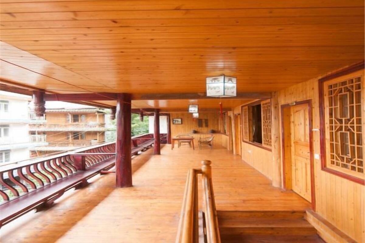 A wooden corridor with benches, a table, and chairs, leading to a balcony with a railing.