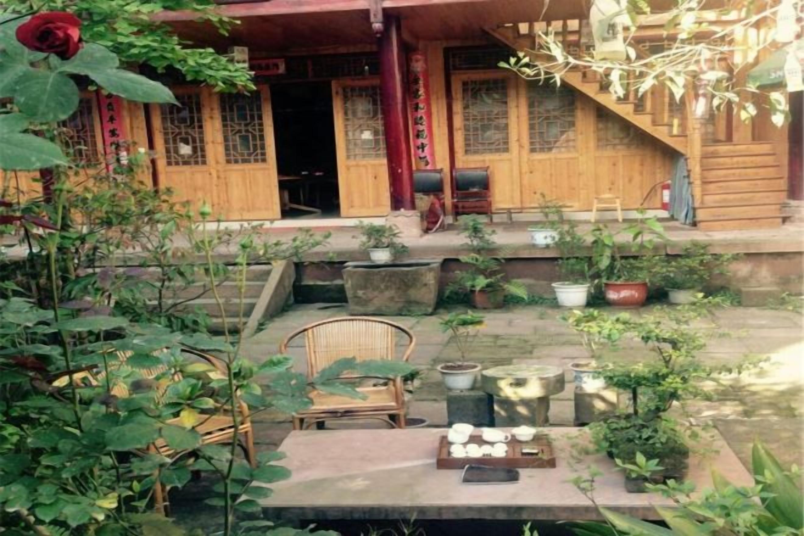 Un edificio de madera tradicional con una escalera que conduce a la entrada, rodeado de plantas en macetas y mobiliario exterior.