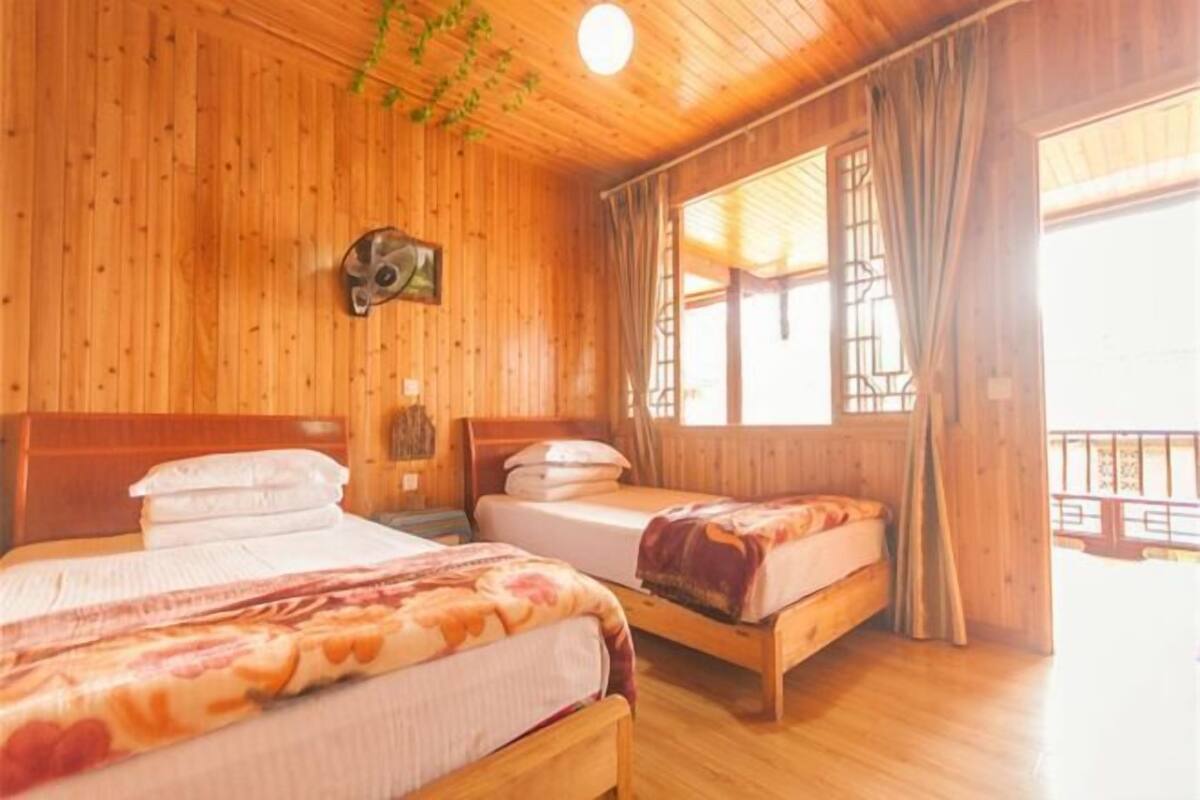 A wooden cabin room with two beds, a wooden ceiling, and a window with curtains.