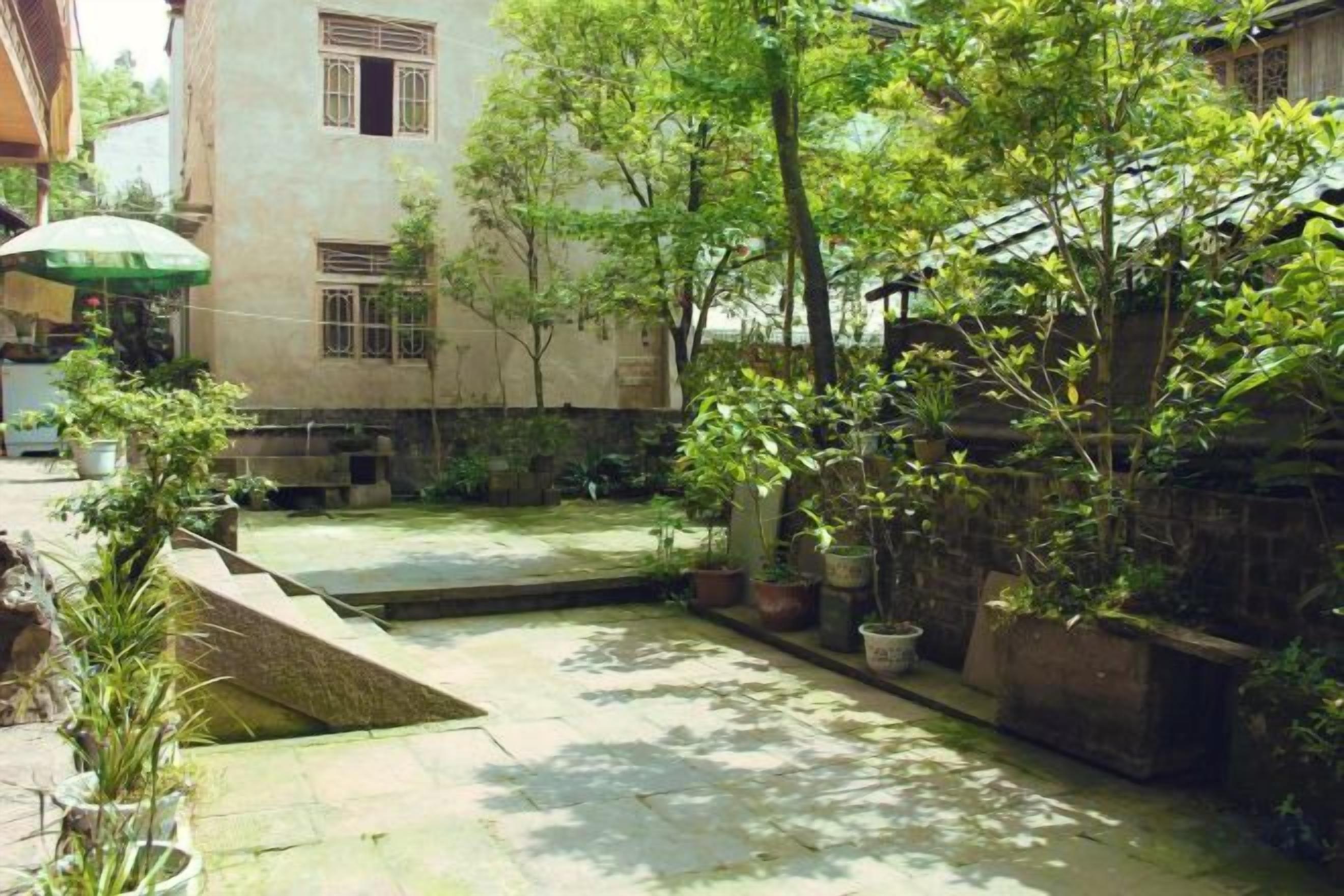 A courtyard with a small water feature, potted plants, and a building with multiple windows.