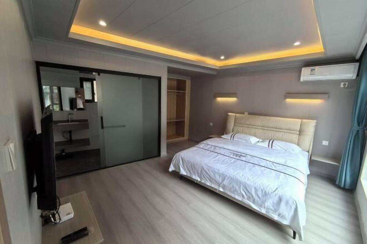 A modern bedroom with a large bed, a television, and a sliding door leading to a bathroom.