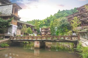 Un puente de madera tradicional sobre un río tranquilo, rodeado de abundante vegetación y edificios tradicionales.