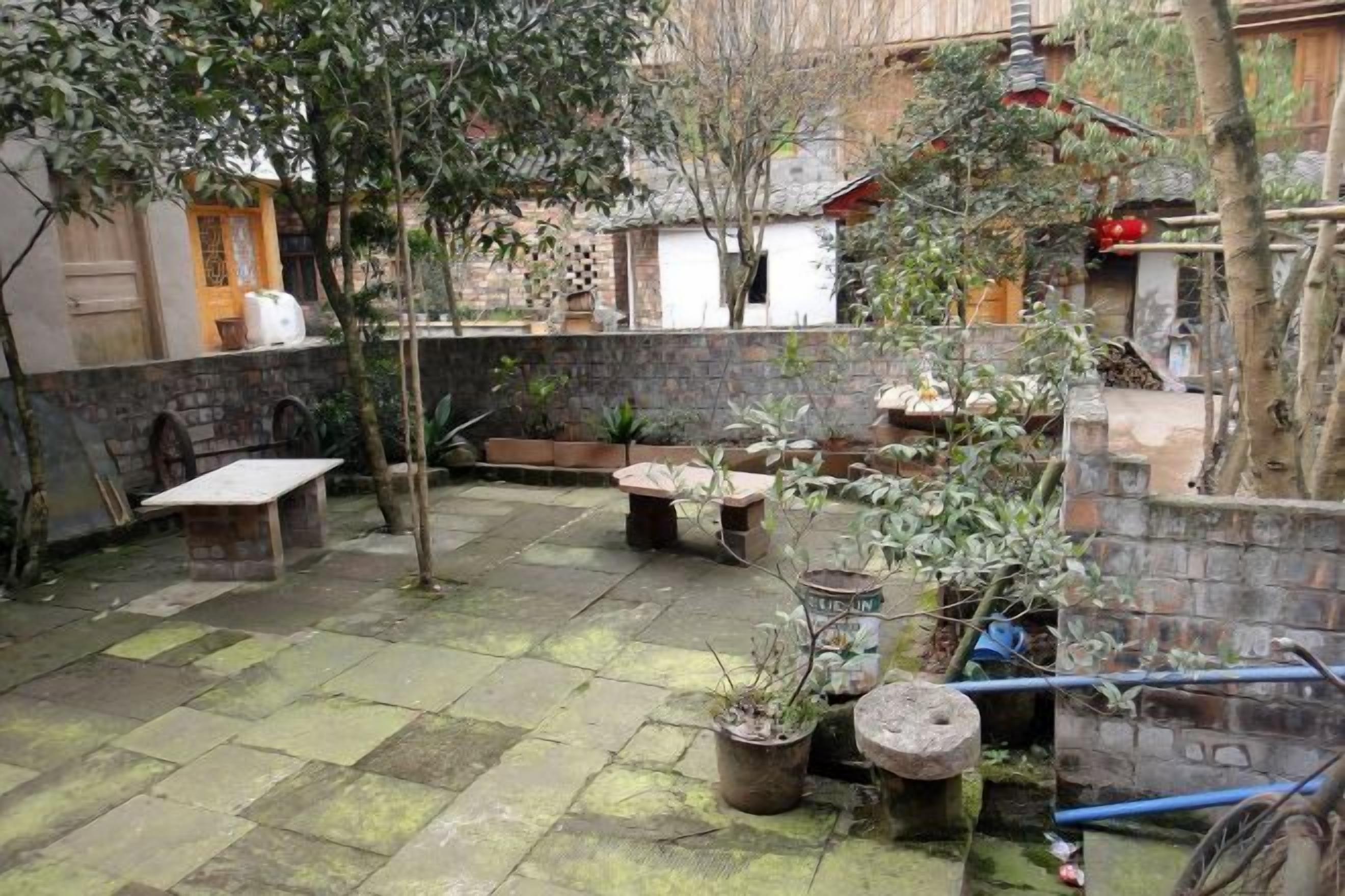 A courtyard with stone flooring, outdoor furniture, potted plants, and a brick wall.