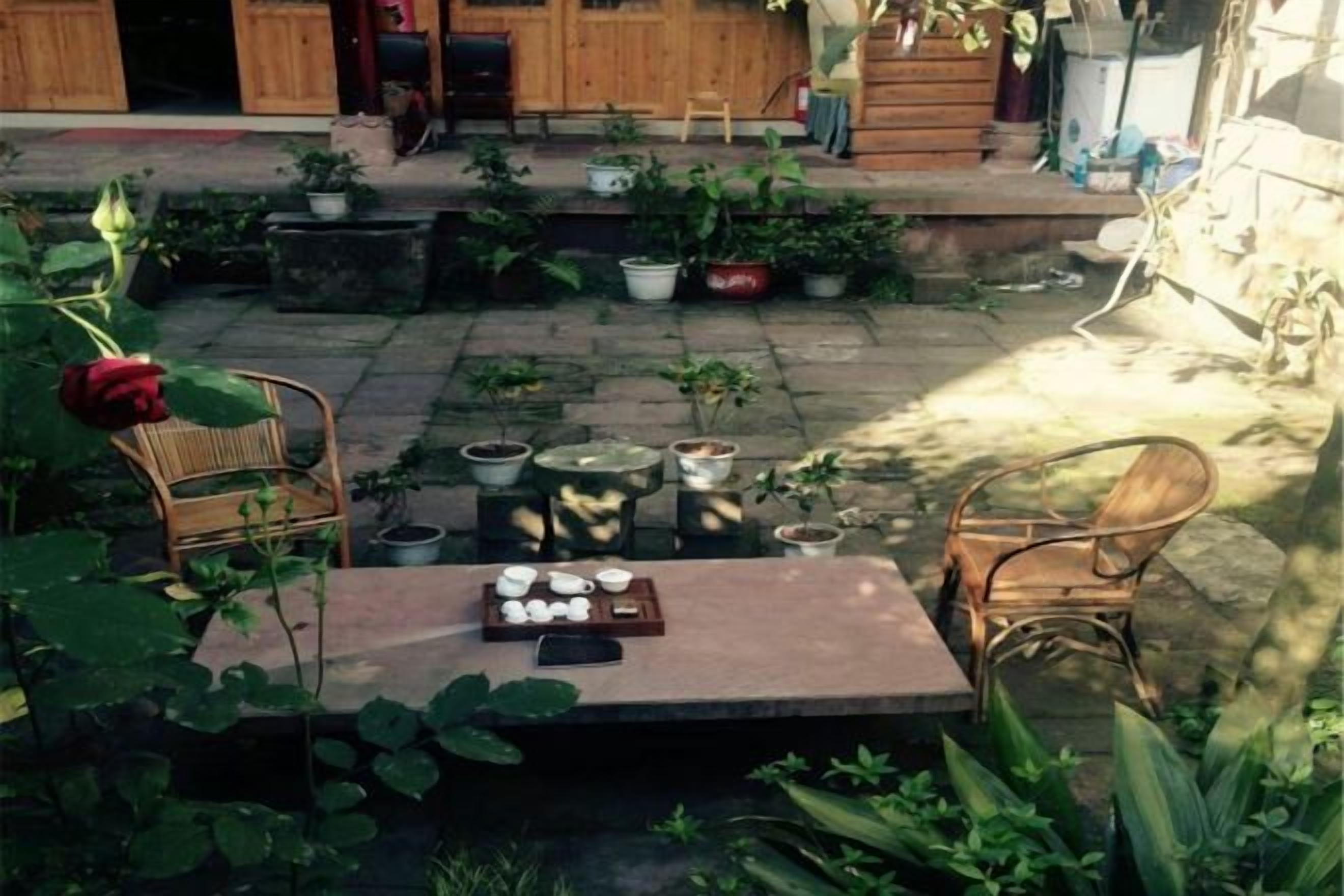 Un patio exterior con una mesa, sillas, plantas en macetas y una valla de madera.
