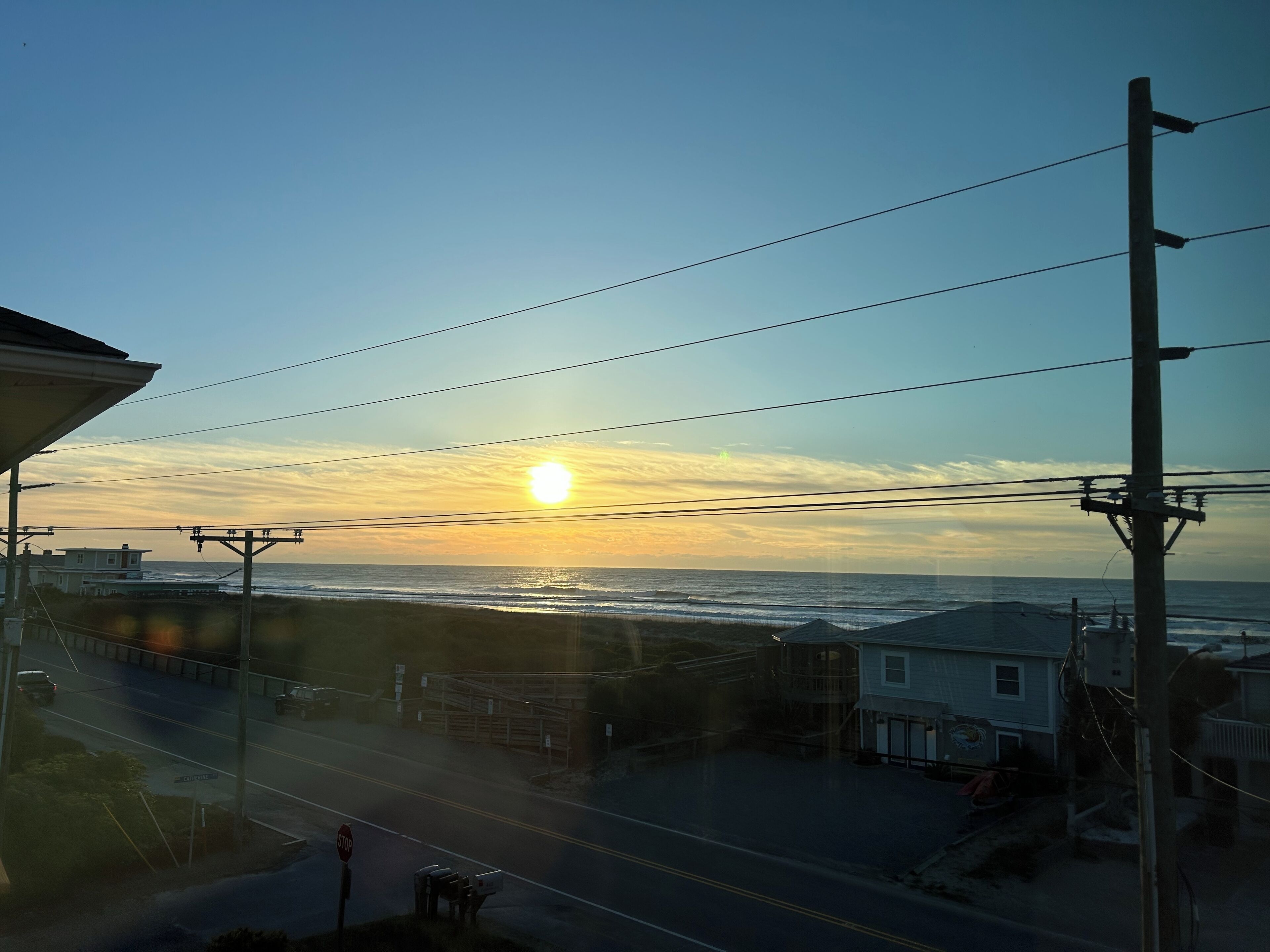 A coastal view with a sunset, power lines, and a stop sign.