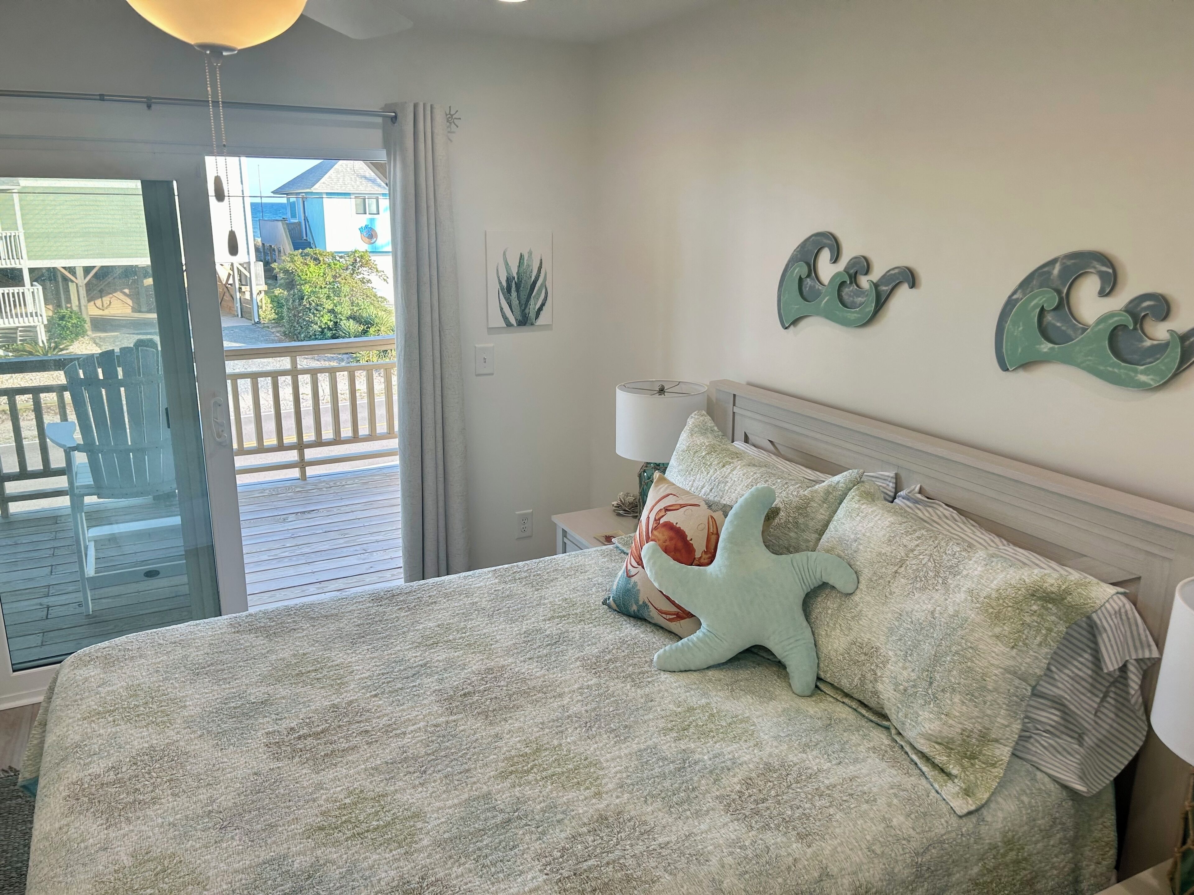 A bedroom with a bed, a nightstand, a lamp, and a view of the outside deck.