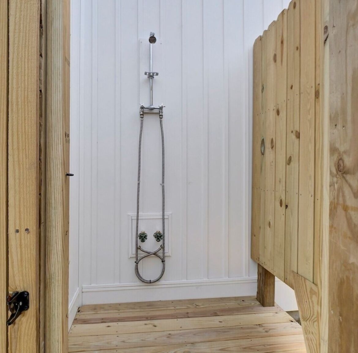 A wooden deck with a white wall and a metal showerhead.
