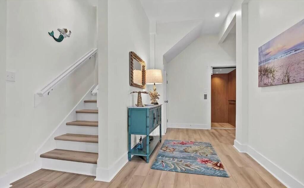 A hallway with a wooden staircase, a teal console table, a mirror, and a floral rug.