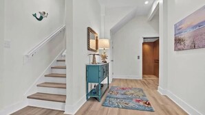A hallway with a wooden staircase, a teal console table, a mirror, and a floral rug. - Bright Beach Escape • Ocean Views • Easy Beach Access (Topsail Beach,)