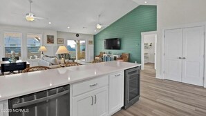 A spacious kitchen with white cabinets, a large island, and a dining area with wicker furniture. - Bright Beach Escape • Ocean Views • Easy Beach Access (Topsail Beach,)