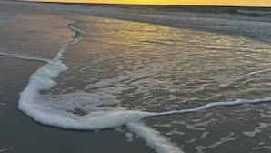 A beach with waves lapping onto the shore and a sunset in the background. - Bright Beach Escape • Ocean Views • Easy Beach Access (Topsail Beach,)