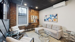 Una sala de estar moderna con una pared de ladrillo, un ventanal grande, un sofá color beige, una mesa de centro de vidrio y un cuadro en la pared.