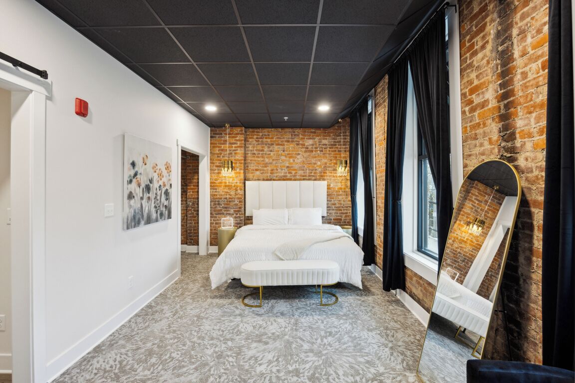 Une chambre moderne avec un mur en briques, un grand lit, un miroir et une vue sur l’extérieur.