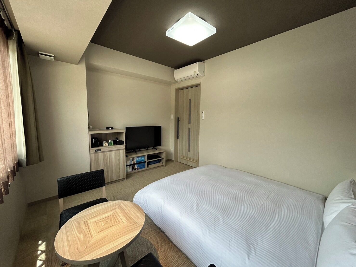 A hotel room with a bed, a TV, a desk with a chair, and a small table.