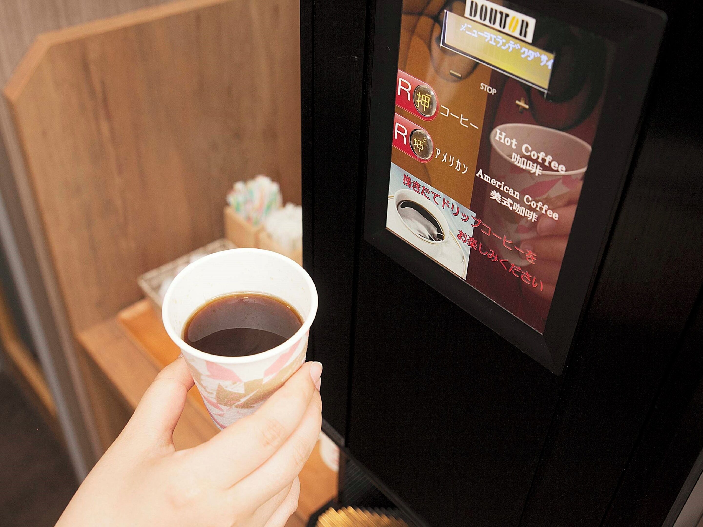 A hand holding a cup of coffee with a digital menu display on a coffee machine.