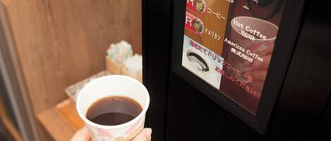 A hand holding a cup of coffee with a digital menu display on a coffee machine.