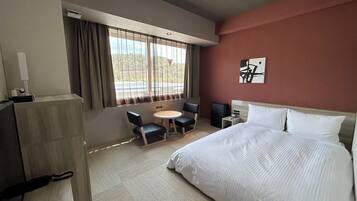 Habitación de hotel con cama, escritorio, silla, mesita y ventana con cortinas.