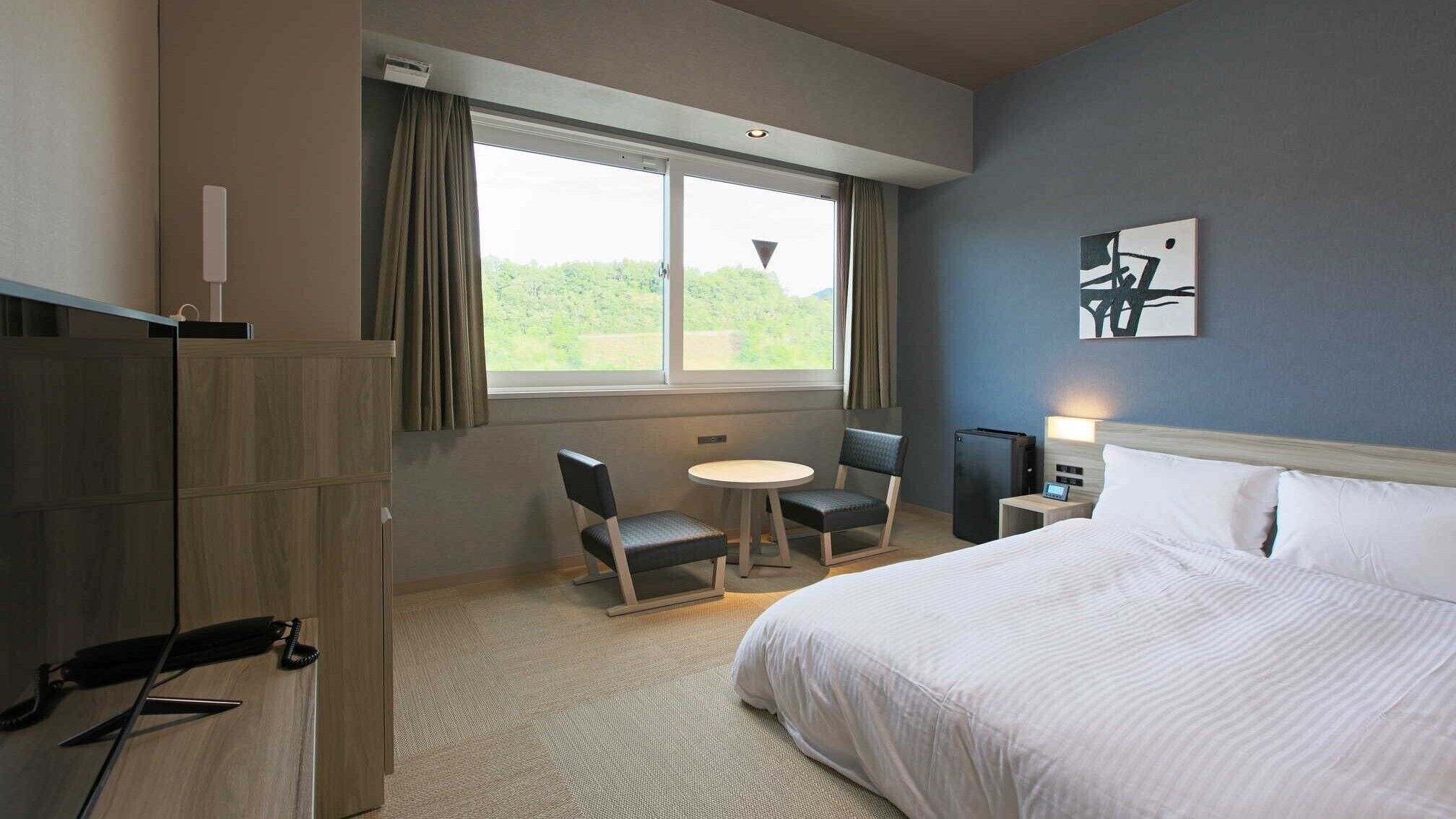 A hotel room with a bed, a desk, a chair, a small table, and a window with curtains.