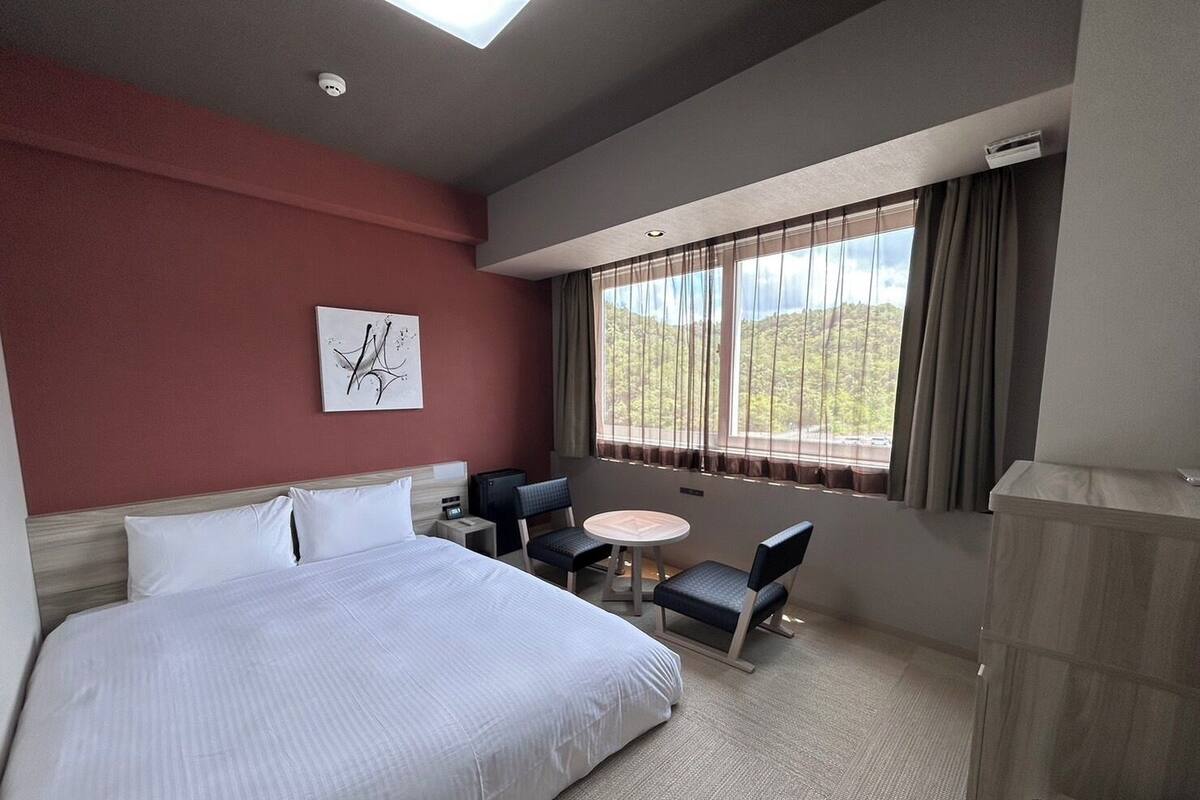 A hotel room with a large bed, a desk, a chair, and a window with curtains.