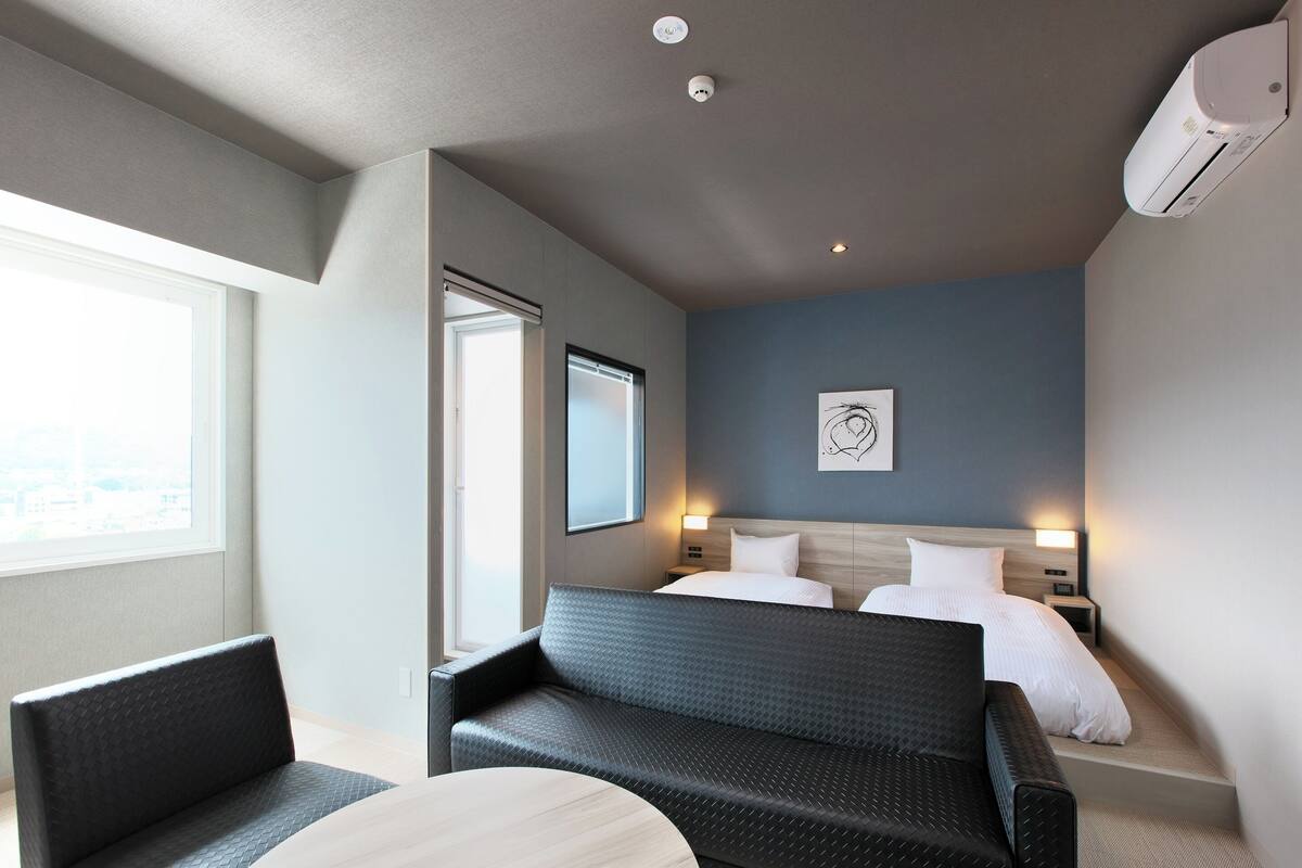 A modern hotel room with a large bed, two bedside tables, a sofa, and a round table.