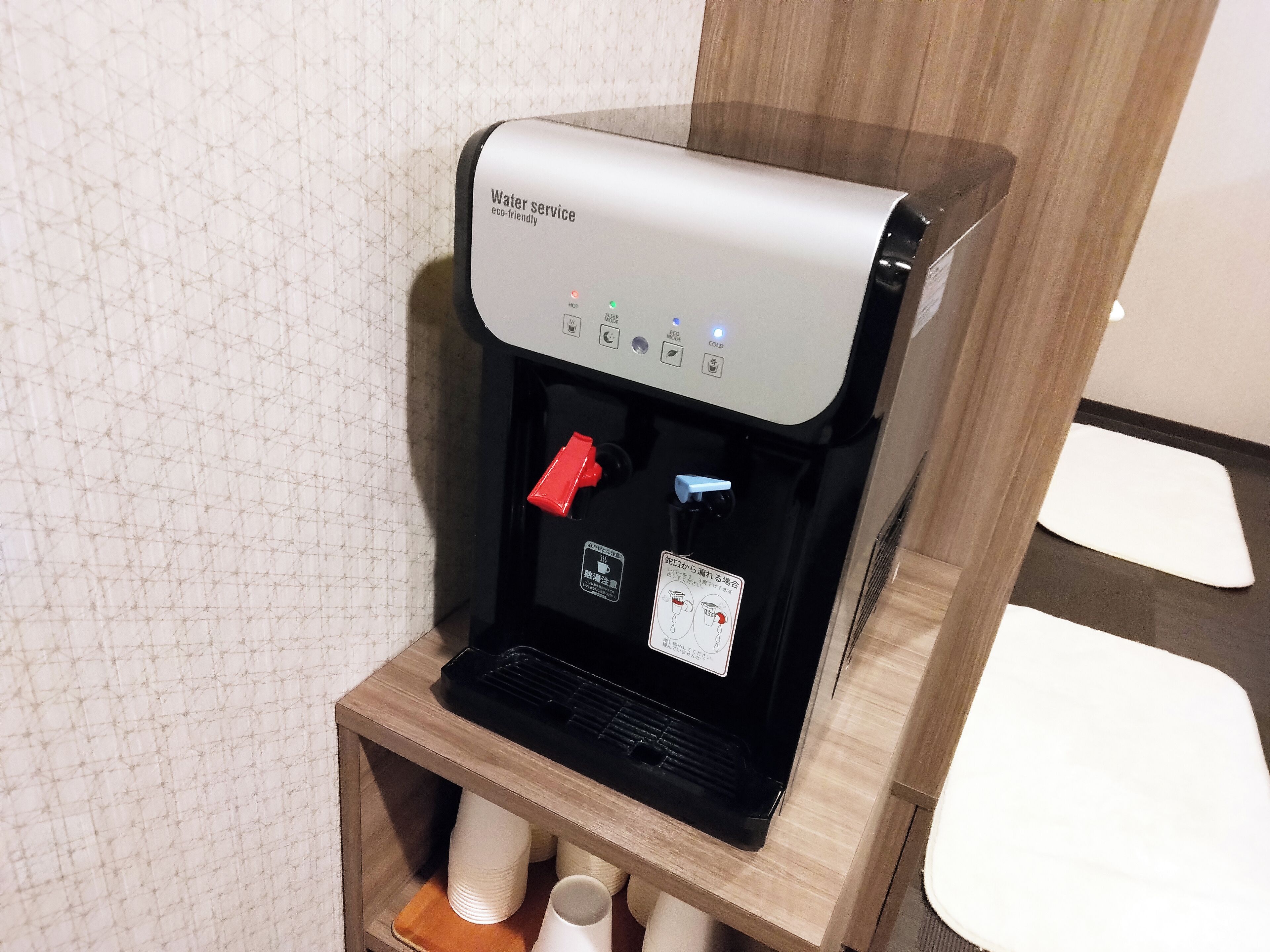 A water dispenser with a control panel, a red button, and a label in a foreign language.