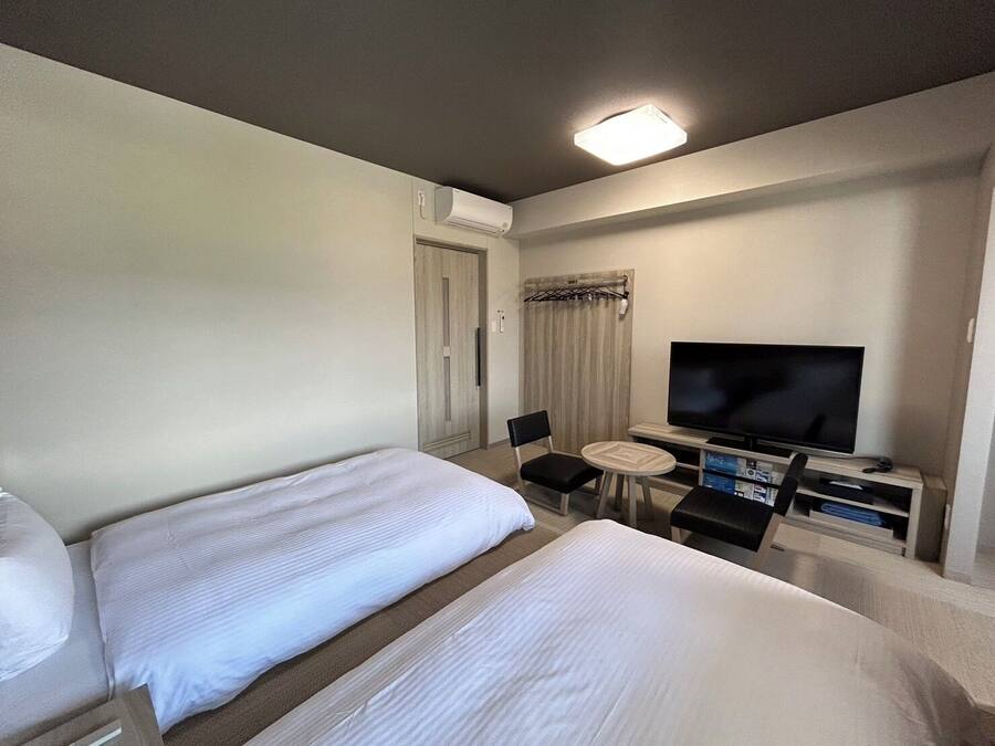 A hotel room with two beds, a television, a small table, and a chair.