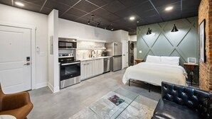 A modern hotel room with a kitchenette, a bed, a glass coffee table, and a leather armchair.