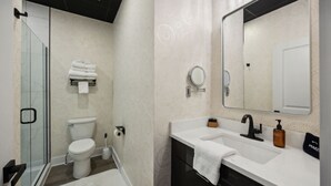 Et moderne badeværelse med brusekabine i glas, toilet, håndvask med spejl og et håndklædestativ.