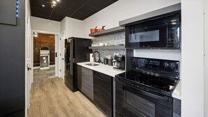 Et moderne køkken med sorte hårde hvidevarer, en hvid bordplade og en murstensvæg.