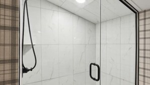 Une salle de bain moderne avec une douche à parois de verre, un mur recouvert de carreaux de marbre blanc et un porte-rouleau de papier toilette visible.