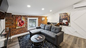 Ein modernes Wohnzimmer mit einem grauen Ecksofa, einem runden Couchtisch und einer Ziegelwand mit großem Fenster.