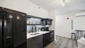 Una cocina moderna con armarios oscuros, un lavamanos de acero inoxidable y un microondas negro. Hay una pequeña zona de comedor con una mesa redonda y dos taburetes.