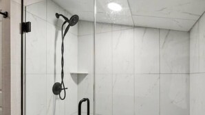 Un área de ducha con paredes de vidrio, un cabezal de ducha manual y un pequeño estante.