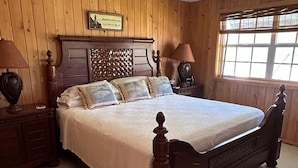 A large bed with a wooden headboard, two bedside tables with lamps, and a window with blinds. - Endless Summer, Cozy Bahamian Cottage (Man o War Cay)