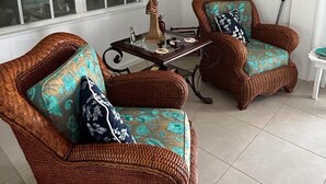 A room with two wicker armchairs with patterned cushions, a small table with a lamp, and a decorative wall piece. - Endless Summer, Cozy Bahamian Cottage (Man o War Cay)