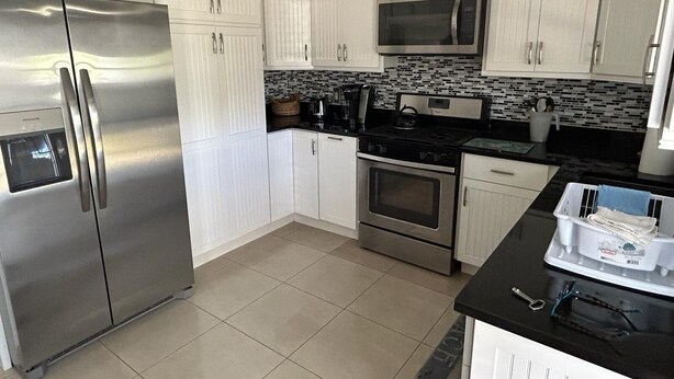 A modern kitchen with white cabinets, stainless steel appliances, and a tiled backsplash. - Endless Summer, Cozy Bahamian Cottage (Man o War Cay)