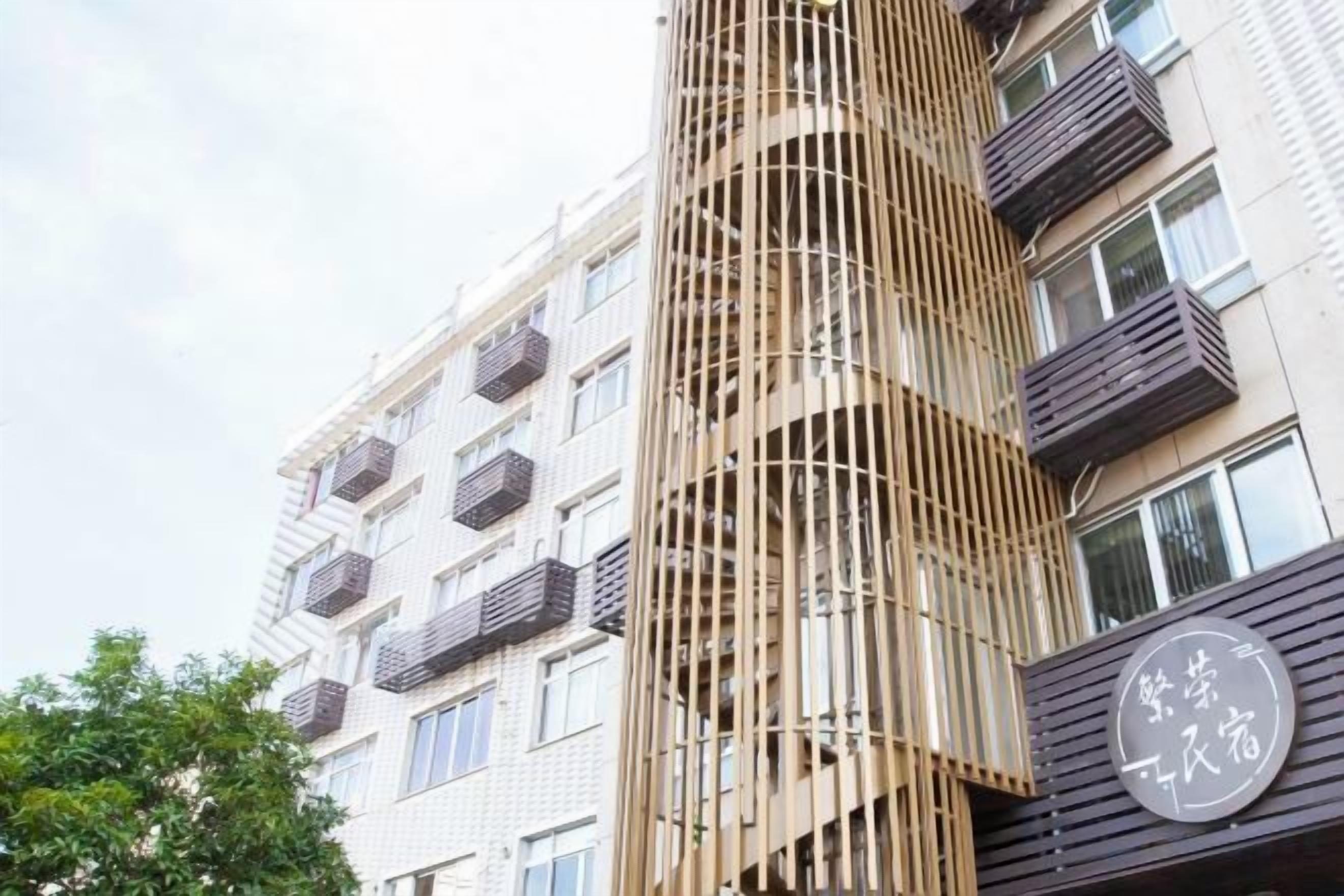 A multi-story building with balconies and a vertical wooden structure.