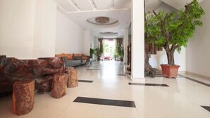 Un vestíbulo amplio con diseño moderno, que incluye un conjunto de sofás, taburetes de madera y una gran planta en maceta.