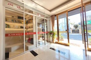 A hotel lobby with a glass door entrance, a reception desk, and a bookshelf with books. - Prosperity Hotel (Yueqing)