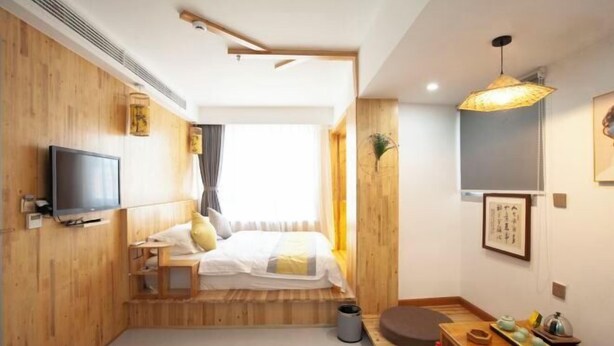 Una habitación de hotel compacta con cama, televisión, detalles de madera, una pequeña mesa con objetos y una lámpara colgante.