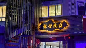 Un edificio con un cartel llamativo en caracteres chinos, una estructura vertical con líneas verticales y un ventanal con cortinas.