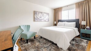 Un dormitorio con cama, una silla, un escritorio y un cuadro en la pared.