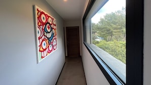 Een smalle gang met een groot abstract schilderij aan de linkerwand, een raam aan de rechterkant en een deur aan het einde.