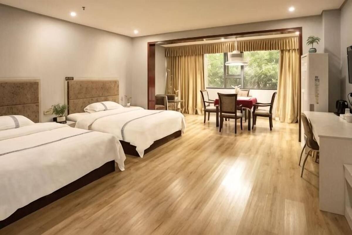A hotel room with two beds, a dining area, and a view of the outdoors.