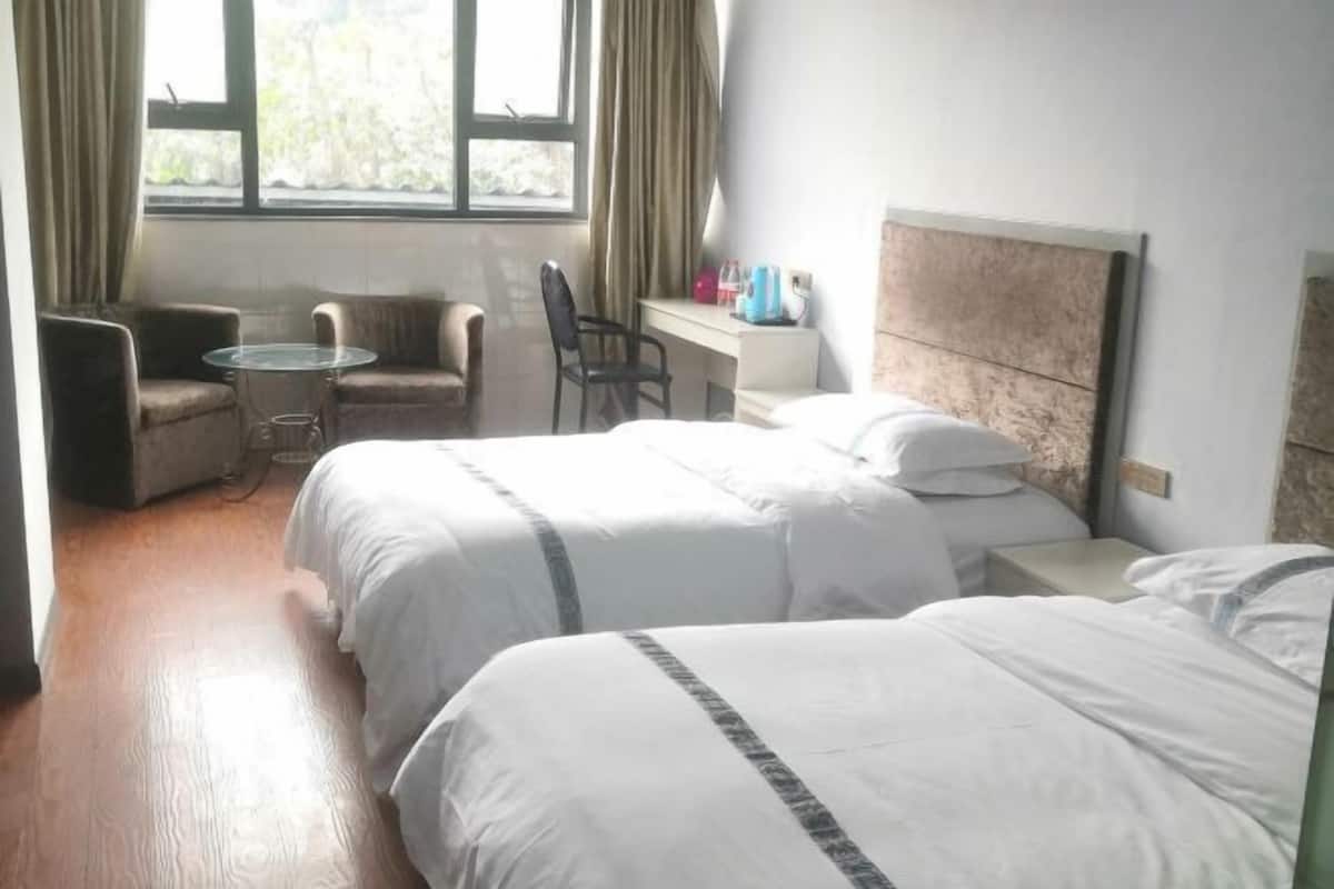 A hotel room with two beds, a small round table, a chair, and a desk with a chair.