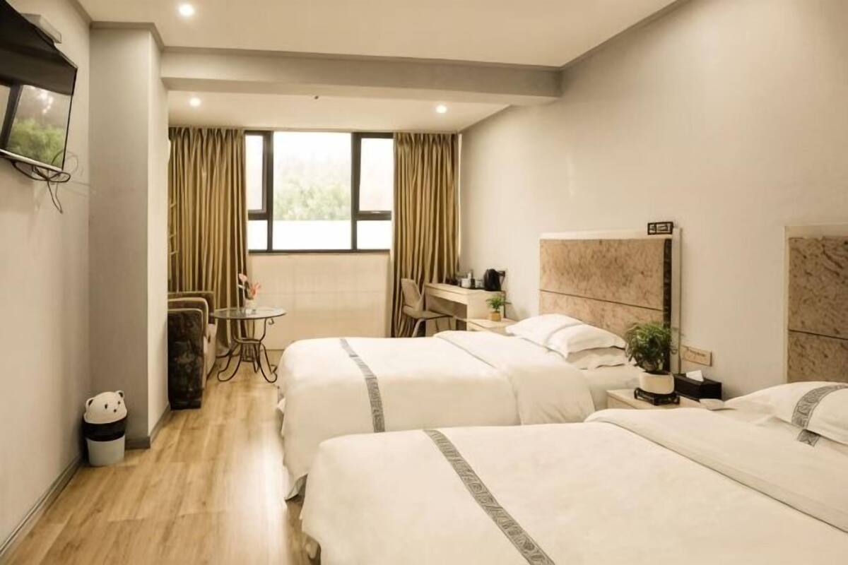 A hotel room with two beds, a desk, a chair, a TV, and a window with curtains.