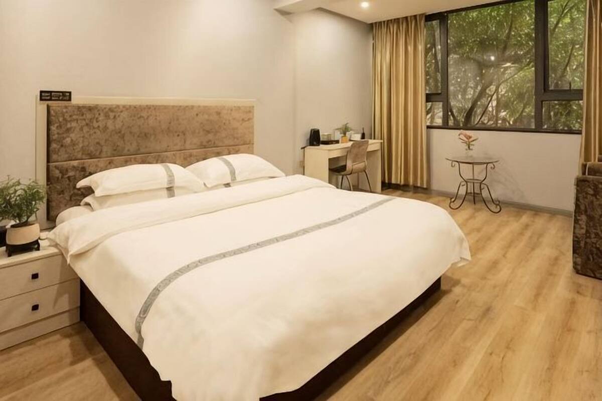 A hotel room with a large bed, a desk, a chair, a small table, and a window with curtains.