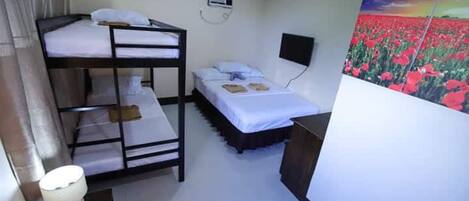 A room with bunk beds, a bedside table with a lamp, a flat-screen TV, and a large painting of a field of flowers.