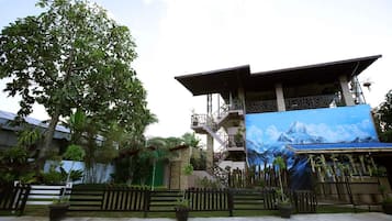 A building with a large mural of a mountain landscape, surrounded by lush greenery and a wooden fence.